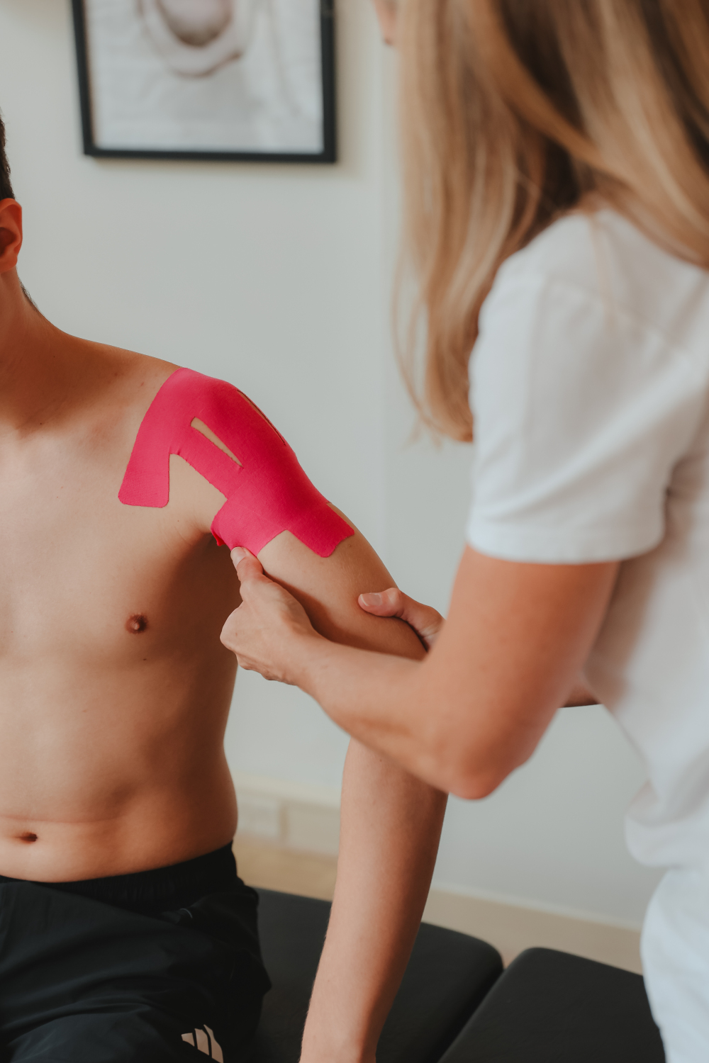 Chiropractor brengt kinesiotape aan op de schouder van een patient